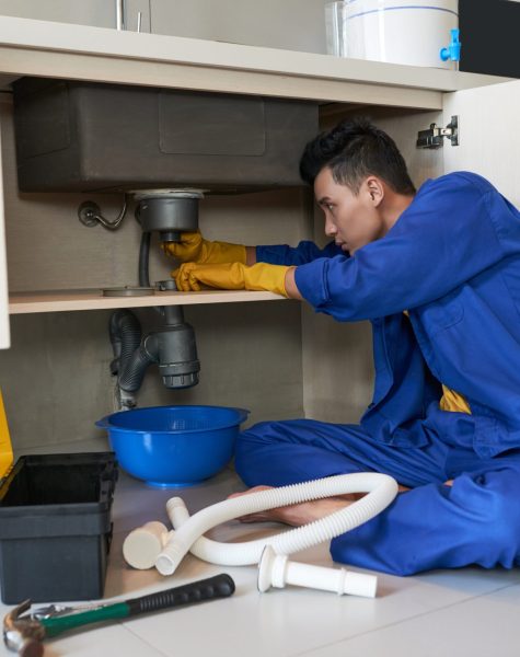 Checking drain Young Vietnamese plumber checking drain in kitchen
