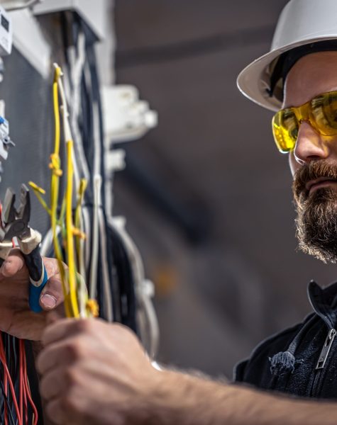 A male electrician works in a switchboard with an electrical connecting cable. Male electrician at the checkout counter on a blurred background of a switchboard.